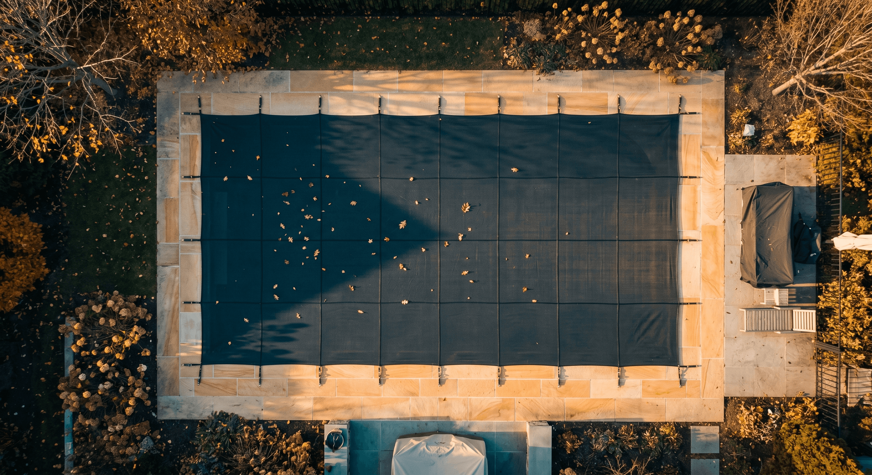 Aerial view of a swimming pool with winter safety cover installed and autumn leaves