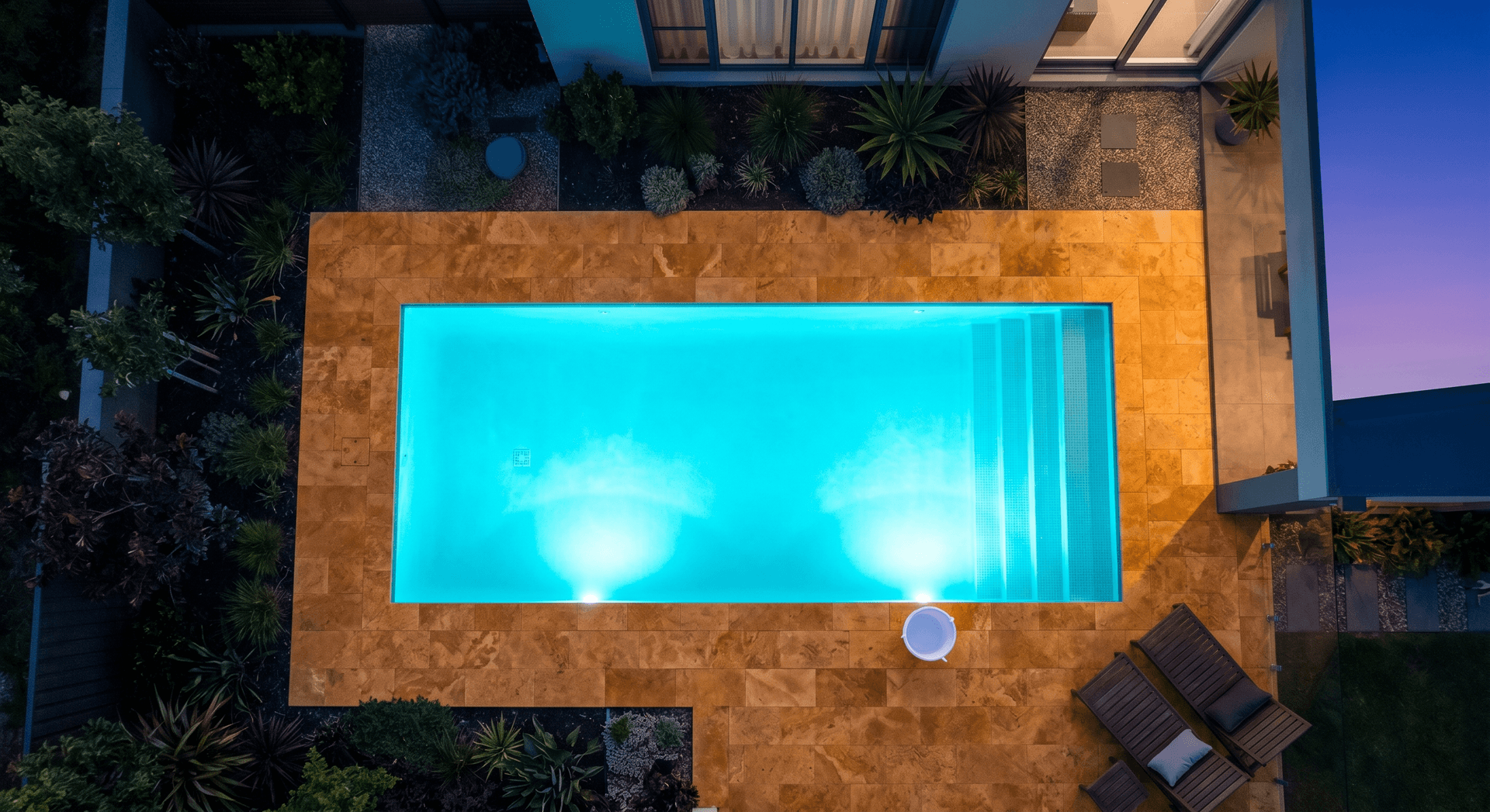Swimming pool at dusk with glowing underwater lights and a white bucket on the deck